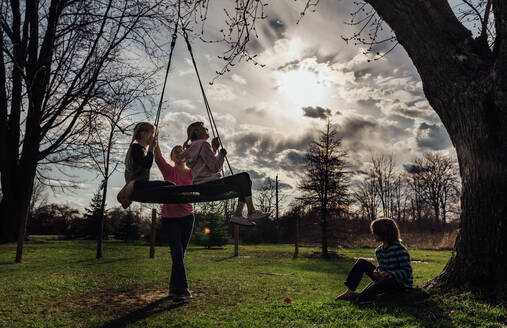 Kinder spielen draußen auf einer Reifenschaukel bei Sonnenuntergang - CAVF86898