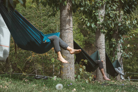 Freunde entspannen sich an einem sonnigen Tag in Hängematten, die an den Bäumen eines Campingplatzes befestigt sind., lizenzfreies Stockfoto