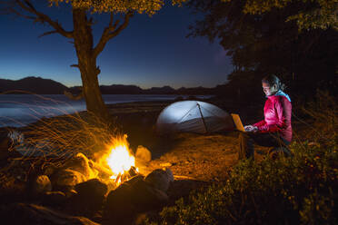 A light painting of a woman doing yoga next to her tent and campfire on a  camping trip along the shores of a lake in Idaho. stock photo