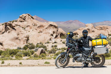 Frau neben Tourenmotorrad auf staubiger Straße in Bolivien stehend - CAVF87025