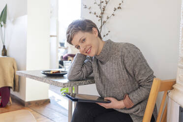 Smiling beautiful woman holding digital tablet while sitting at coffee shop - TAMF02503