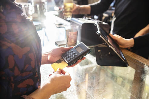 Weiblicher Kunde, der an der Kasse eines Cafés mit Kreditkarte bezahlt - TAMF02507