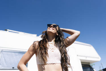 Junge Frau mit Sonnenbrille vor einem Wohnmobil - JCMF00969