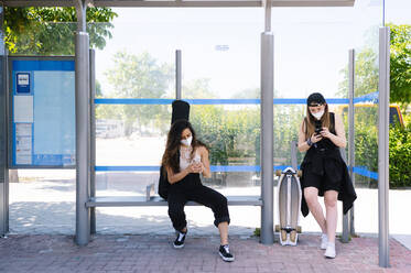Zwei Frauen mit Gesichtsschutzmasken warten am Busbahnhof - JCMF00973