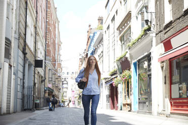 Smiling woman exploring city while walking on footpath amidst buildings - PMF01151