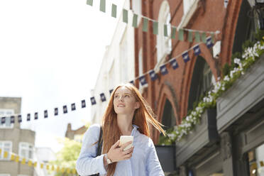 Beautiful woman looking away while walking with smart phone against building in city - PMF01164