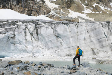 Älterer männlicher Wanderer mit Blick auf den schmelzenden Gletscher - MCVF00503