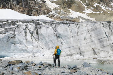 Mann beim Wandern mit Blick auf den schmelzenden Gletscher - MCVF00504