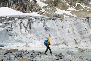 Männlicher Wanderer, der auf Felsen stehend den schmelzenden Gletscher erkundet - MCVF00505