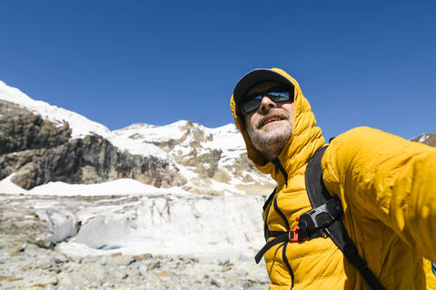 Smiling mature man standing against snowcapped mountain stock photo