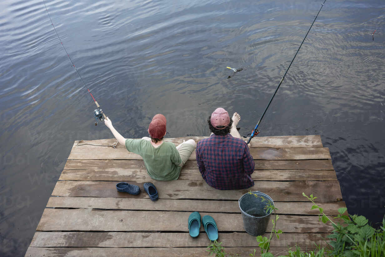 Teen boy fishing from a dock on a lake with brothers swimming