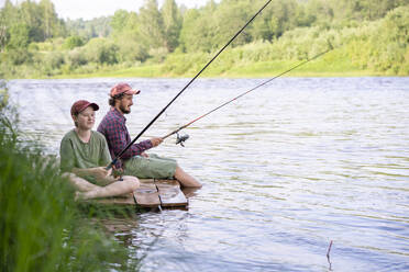 Vater und Sohn beim Angeln am Flussufer sitzend - VPIF02606