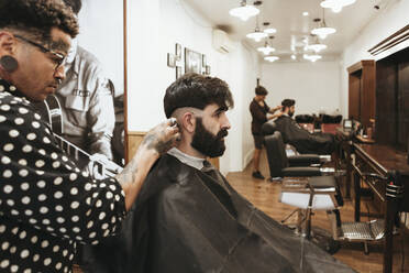 Trendiger Friseur, der die Haare eines Kunden im Salon stylt - XLGF00364