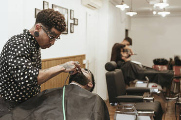 Trendiger Friseur stylt den Bart eines Kunden im Salon - XLGF00374
