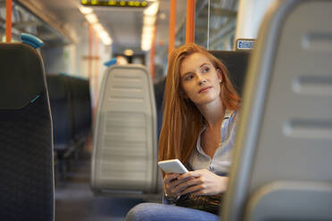 Nachdenkliche Frau mit Smartphone im Zug sitzend - PMF01175