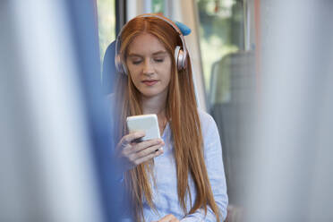 Beautiful young woman listening music while sitting in train - PMF01176
