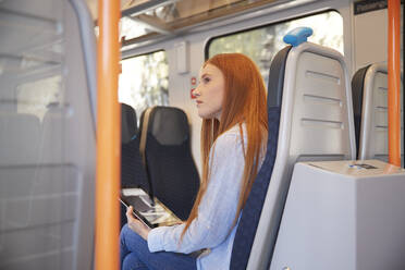 Thoughtful woman holding digital tablet while sitting in train - PMF01177