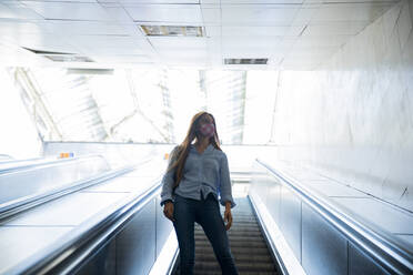 Young woman wearing mask while standing on escalator at subway station - PMF01182