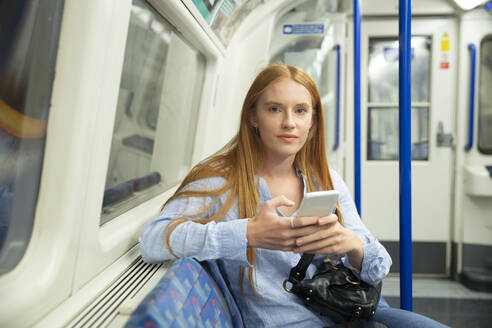 Schöne Frau hält Smartphone im Zug sitzend - PMF01185