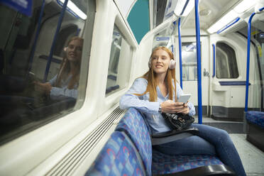 Beautiful young woman looking through window while listening music in train - PMF01187