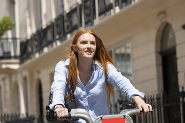 Beautiful woman riding hire bike in city during sunny day - PMF01200