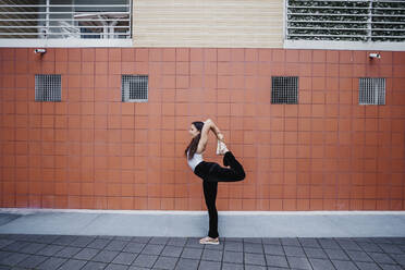 Junge Frau beim Yoga auf dem Gehweg vor einer gekachelten Wand in der Stadt - MEUF01298
