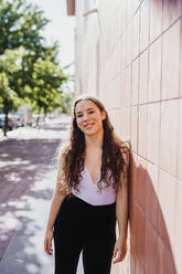 Happy sporty woman leaning on tiled wall during sunny day - MEUF01301