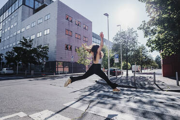 Aufgeregte junge Frau springt an einem sonnigen Tag auf einer Straße in der Stadt - MEUF01303