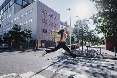 Excited young woman jumping on city street during sunny day - MEUF01303