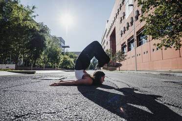 Junge Frau beim Yoga auf der Straße in der Stadt an einem sonnigen Tag - MEUF01305