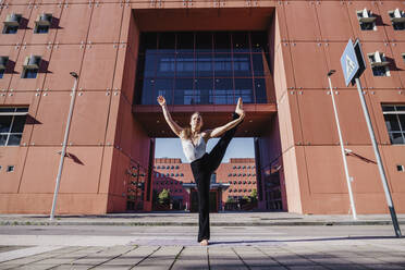 Junge Frau, die Yoga in der Hand zum großen Zeh Pose auf der Straße der Stadt - MEUF01307