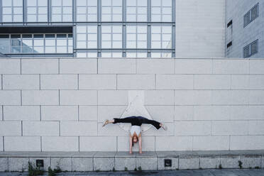 Young woman performing handstand on sidewalk against tiled wall in city - MEUF01309