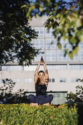 Entspannte junge Frau übt Yoga in Gebetshaltung, während sie im Stadtpark auf dem Rasen sitzt - MEUF01320