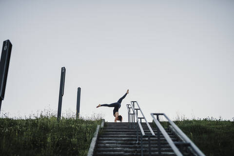 Young woman performing handstand on steps against clear sky stock photo