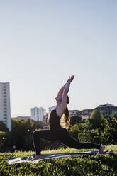 Junge Frau übt Yoga in der Position des Kriegers im Stadtpark gegen den klaren Himmel - MEUF01324