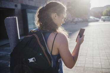 Sporty young woman using smart phone while walking on city street during sunny day - MEUF01337