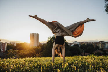 Junge Frau macht Handstand im Stadtpark bei Sonnenuntergang - MEUF01349