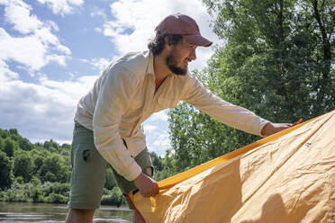 Mittlerer Erwachsener, der sein Zelt im Wald gegen den Himmel auf dem Campingplatz aufbaut - VPIF02613