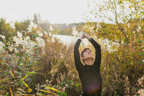 Woman with arms raised exercising while standing amidst plants against clear sky stock photo