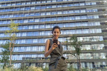 Geschäftsfrau, die ein Mobiltelefon benutzt, während sie an einem Gebäude in der Stadt steht - AFVF06724