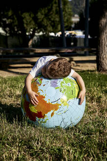 Boy embracing globe on grassy land in park during sunny day - VEGF02515