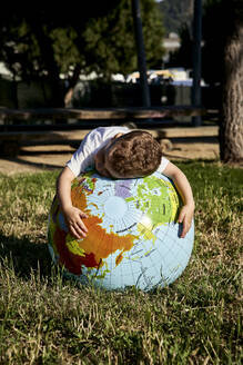 Junge umarmt Globus auf grasbewachsenem Gelände im Park an einem sonnigen Tag - VEGF02515