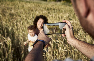 Nahaufnahme eines Mannes, der Mutter und Sohn mit einem Smartphone auf einem Bauernhof fotografiert - VEGF02526