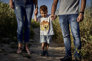 Son holding parents hands while standing on trail amidst crops in farm - VEGF02530