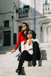 Stilvolle Freundinnen mit Sonnenbrillen sitzen auf den Stufen eines Gebäudes in der Stadt - DCRF00359