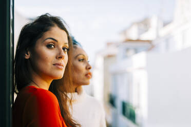 Thoughtful female friends looking away while standing in balcony - DCRF00360