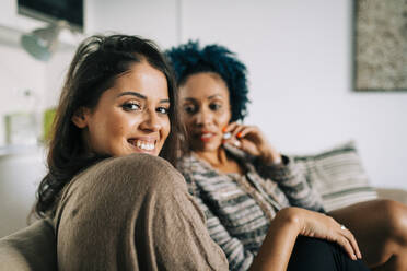 Smiling young woman with friend sitting on sofa at home - DCRF00386