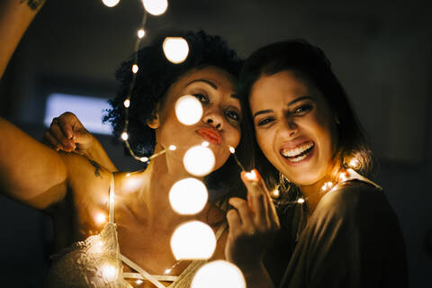 Close-up of happy female friends holding illuminated string lights at home stock photo