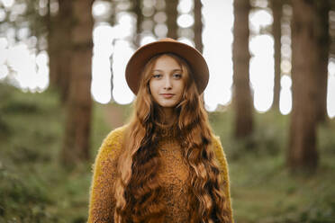 Beautiful woman with long hair wearing hat standing in forest - TCEF00933