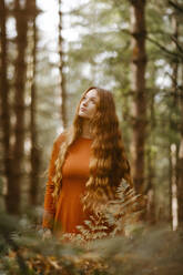 Nachdenkliche schöne Frau mit langen Haaren im Wald stehend - TCEF00936